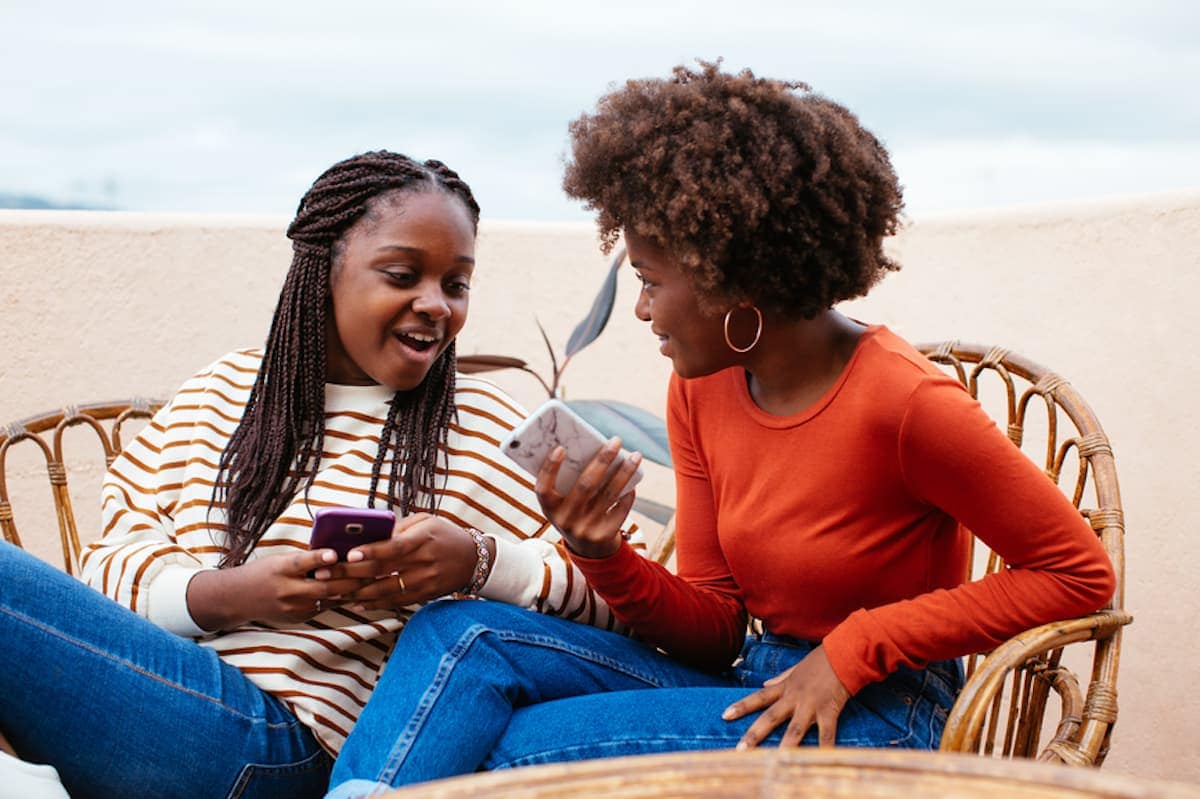 Две молодые женщины на пляже смотрят на мобильные телефоны