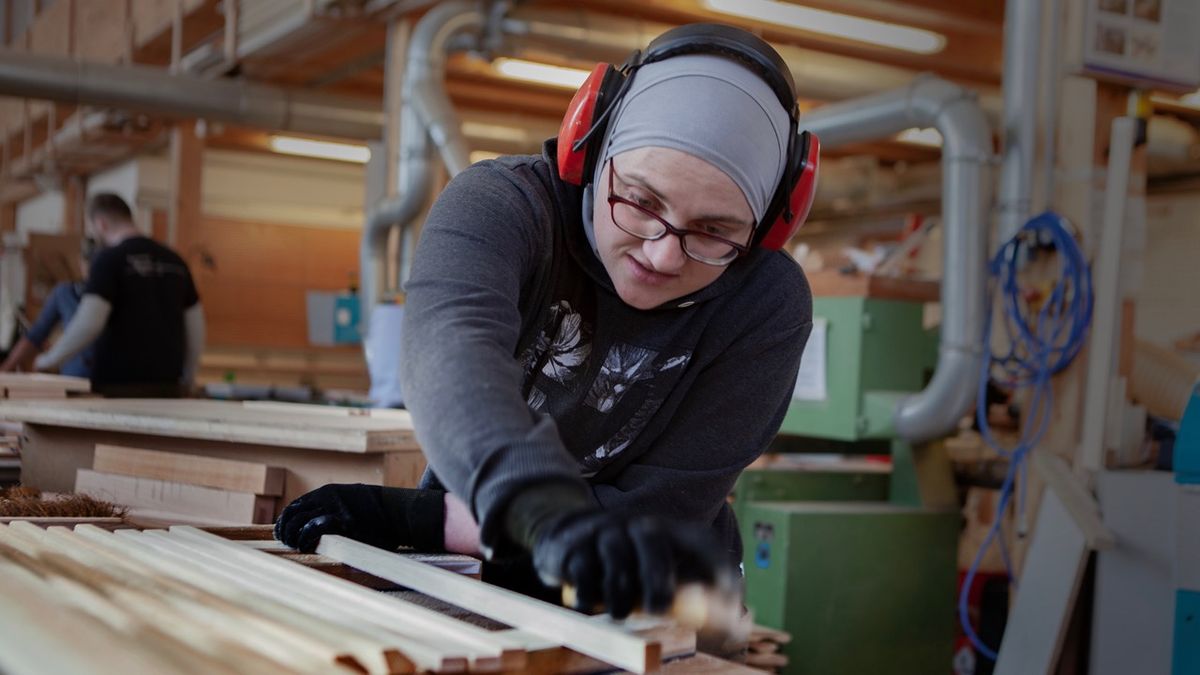 Женщина в столярке шлифует доску с наушниками